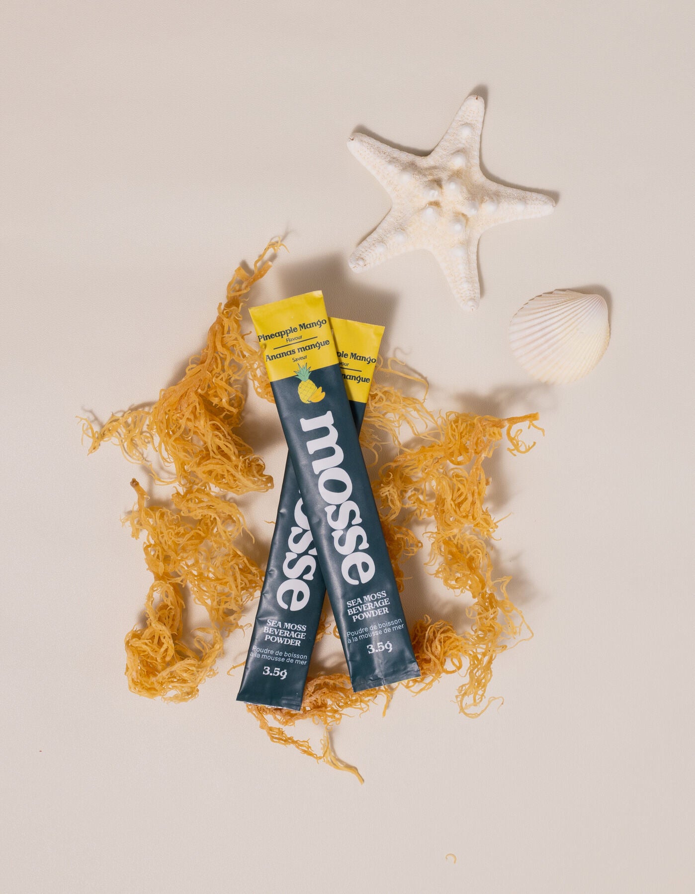 sea moss two stick packs on sand background with raw sea moss and shells